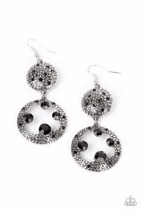 Dotted with dainty black rhinestones and embossed in pebble-like textures, a beveled silver circle attaches to an imperfect silver hoop featuring matching texture. A smattering of oversized black rhinestones haphazardly adorns the hoop, resulting in a gritty shimmer. Earring attaches to a standard fishhook fitting.  Sold as one pair of earrings.