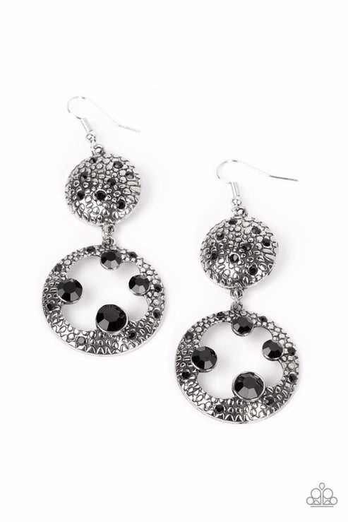 Dotted with dainty black rhinestones and embossed in pebble-like textures, a beveled silver circle attaches to an imperfect silver hoop featuring matching texture. A smattering of oversized black rhinestones haphazardly adorns the hoop, resulting in a gritty shimmer. Earring attaches to a standard fishhook fitting.  Sold as one pair of earrings.