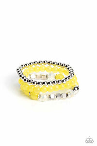 Varying in shape and size, shiny silver beads, silver cube beads, silver accents, primrose opaque beads, and reflective crystal-like beads are threaded along elastic stretchy bands, creating colorful layers across the wrist.  Sold as one set of three bracelets.