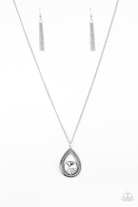 An oversized white rhinestone is nestled inside the bottom of a glistening silver teardrop radiating with studded textures. The dramatic pendant swings from the bottom of a lengthened silver chain for a regal look. Features an adjustable clasp closure.  Sold as one individual necklace. Includes one pair of matching earrings.