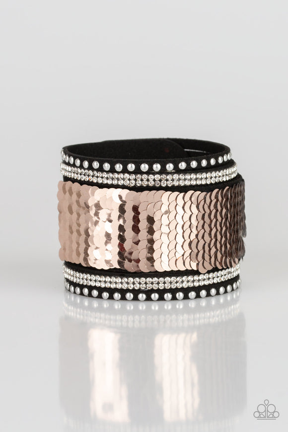 Shiny silver studs, glassy white rhinestones, and shimmering sequins are sprinkled across a thick black suede band that has been spliced into five glittery rows. Bracelet features reversible sequins that change from silver to rose gold. Features an adjustable snap closure.  Sold as one individual bracelet.