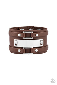 A collection of leather pieces and shiny silver frames are studded in place across the front of a thick leather band, creating an abstract buckle. Features an adjustable snap closure.  Sold as one individual bracelet.