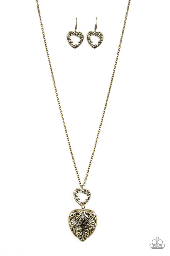 Swirling with ornate floral filigree details, a pair of brass heart frames link at the bottom of a lengthened brass chain for a vintage inspired look. Features an adjustable clasp closure.  Sold as one individual necklace. Includes one pair of matching earrings.