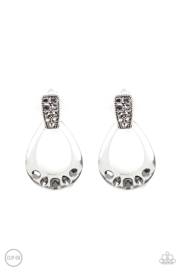 The bottom of a shimmery silver teardrop frame is encrusted in a mismatched collection of smoky and hematite rhinestones as it swings from the bottom of a hematite rhinestone encrusted fitting for a refined flair. Earring attaches to a standard clip-on fitting.  Sold as one pair of clip-on earrings.