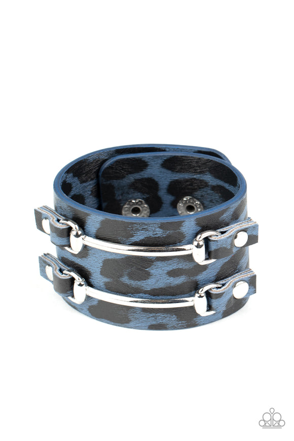Two arcing silver bars are studded in place across the front of a thick leather band painted in blue and black cheetah print for a wild look. Features an adjustable snap closure.  Sold as one individual bracelet.