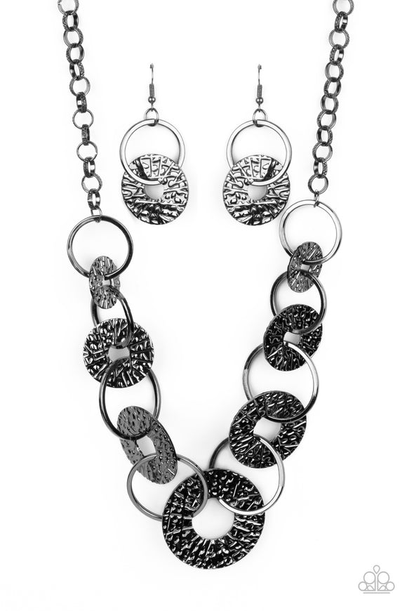 Gradually increasing in size near the center, a collection of glistening gunmetal rings and abstract hammered discs interlock below the collar for an intense industrial look. Features an adjustable clasp closure.  Sold as one individual necklace. Includes one pair of matching earrings.