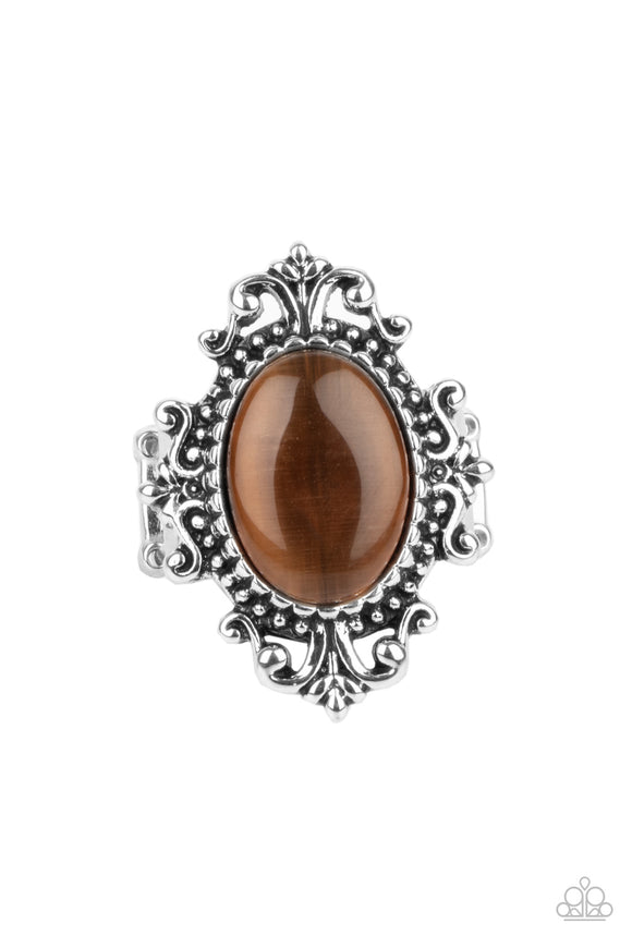 A glowing brown cat's eye stone is pressed into the center of an ornately studded silver frame, creating a mystical pop of color atop the finger. Features a stretchy band for a flexible fit.  Sold as one individual ring.