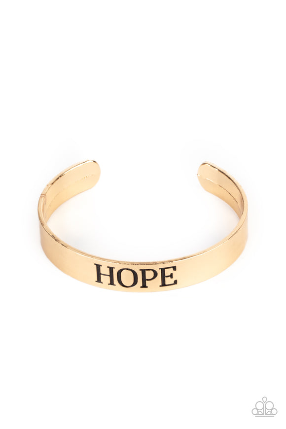 The center of a shiny gold cuff is stamped in the word, 