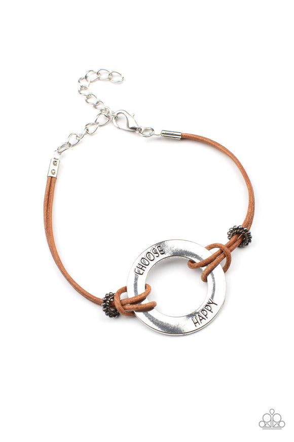 Infused with antiqued studded beads, brown leathery cords knot around a silver ring stamped in the phrase, 