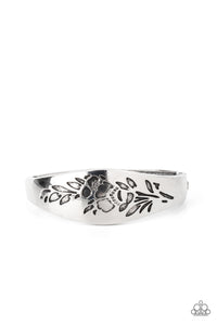 The front of a thick antiqued silver bangle-like bracelet is stamped in a leafy floral pattern, creating a whimsy centerpiece around the wrist. Features a hinged closure.  Sold as one individual bracelet.