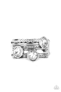 A trio of oversized white rhinestones haphazardly adorns layers of mismatched rows of dainty white rhinestones and antiqued silver bands, coalescing into a knockout centerpiece. Features a stretchy band for a flexible fit.  Sold as one individual ring.