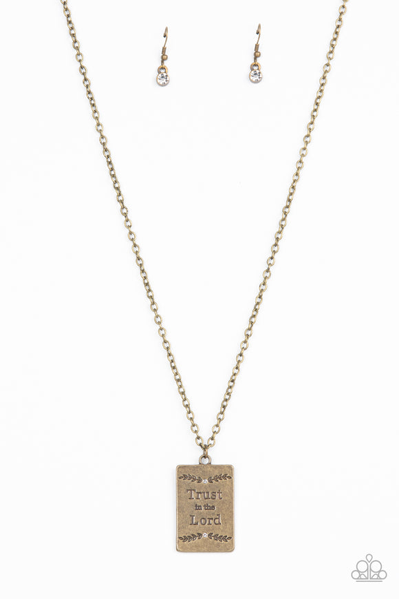 Bordered in leafy patterns and dainty white rhinestones, the center of a rectangular brass frame is stamped in the phrase, 