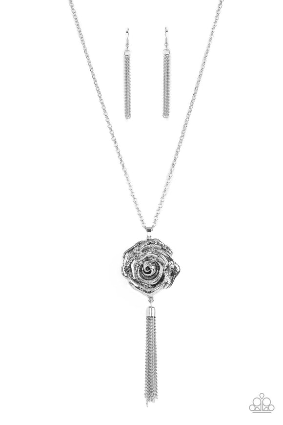 A rustic silver chain tassel dances from the bottom of an oversized silver rosebud frame, resulting in a vintage inspired pendant at the bottom of an extended silver chain. Features an adjustable clasp closure.  Sold as one individual necklace. Includes one pair of matching earrings.