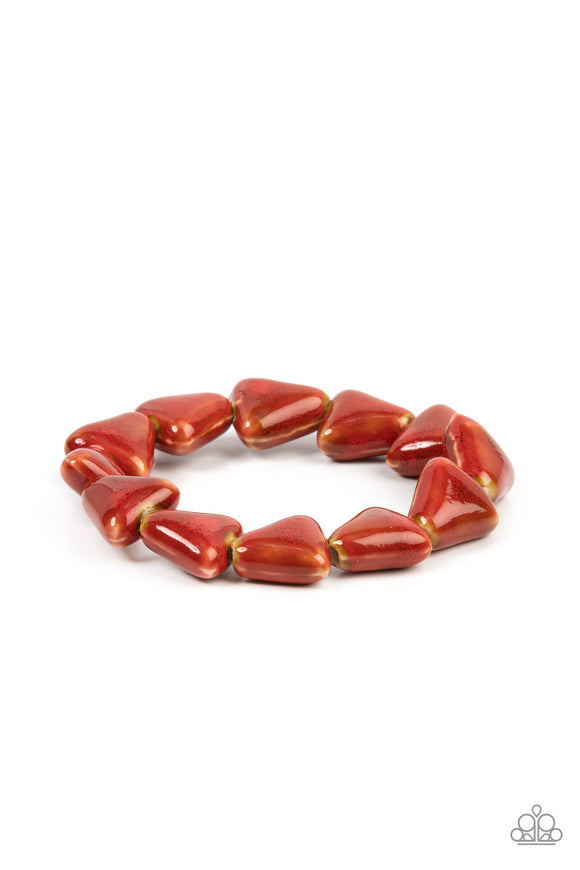 Painted in a distressed red finish, ceramic beads shaped like shark teeth are threaded along a stretchy band around the wrist for a seasonal flair.  Sold as one individual bracelet.