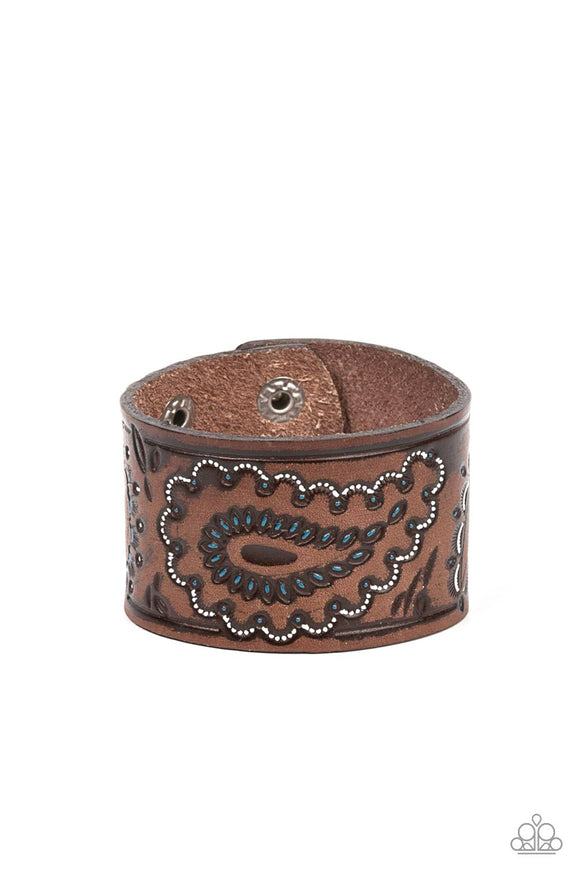 Highlighted in white and blue paint, a rustic paisley pattern is stamped across the front of a distressed leather band for a rustic flair. Features an adjustable snap closure.  Sold as one individual bracelet.