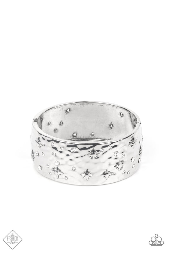 A wide silver band, hammered with subtle texture, is sprinkled with a constellation of embossed silver stars and sparkling dainty white rhinestones, creating a heavenly display around the wrist. Features a hinged closure.  Sold as one individual bracelet.
