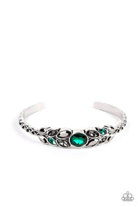 A large green rhinestone is set in a rounded silver frame and set atop a skinny silver cuff. Marquise shaped pieces of hematite, green rhinestones and rhinestones in a smoky hue fan out from the center in a leafy pattern, giving way to bars of silver adorned in a linked texture.  Sold as one individual bracelet.