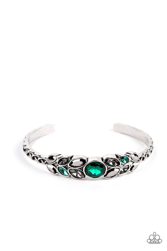 A large green rhinestone is set in a rounded silver frame and set atop a skinny silver cuff. Marquise shaped pieces of hematite, green rhinestones and rhinestones in a smoky hue fan out from the center in a leafy pattern, giving way to bars of silver adorned in a linked texture.  Sold as one individual bracelet.