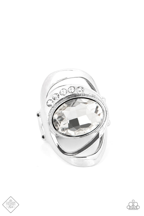 An oversized white oval gem is tilted on its side and nestled into a sleek silver frame. A row of dainty white rhinestones runs along the edge of the faceted centerpiece, as a larger silver frame ripples out from underneath, creating an abstract and modern statement piece. Features a stretchy band for a flexible fit.  Sold as one individual ring.