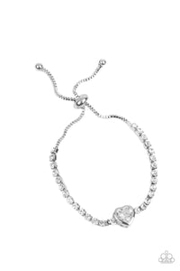 A strand of tiny white rhinestones, encased in silver, square fittings, leads to a white, heart-shaped gem wrapped in a sleek, three-dimensional, silver frame. The glittery display connects to a dainty silver box chain with silver beads on each end, wrapping around the wrist in a romantic finish. Features an adjustable sliding bead closure.  Sold as one individual bracelet.