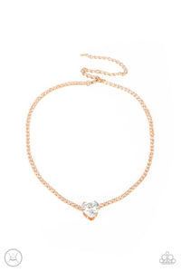 An oversized white heart-shaped gem, set in an airy, pronged gold fitting, glitters at the center of a blinding row of dainty, glassy white rhinestones set in square gold fittings, resulting in a flirtatious sparkle around the neckline. Features an adjustable clasp closure.  Sold as one individual choker necklace. Includes one pair of matching earrings.