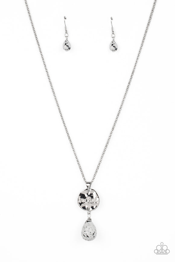 Swinging from a dainty silver chain, a hammered disc in the same hue is stamped with the words 