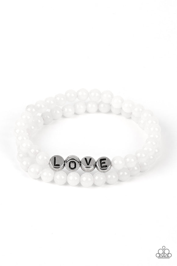 Cloudy beads in subtle shades of white extend around the wrist on elastic stretchy bands for a two-for-one romantic stack. Centered on one of the white bracelets, silver discs stamped with individual black letters spell out the word 
