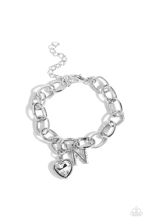 A simple collection of silver charms — including a white rhinestone heart pressed in a silver frame and a sleek letter 