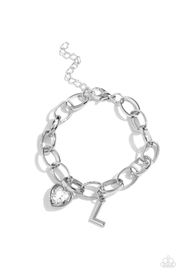 A simple collection of silver charms — including a white rhinestone heart pressed in a silver frame and a sleek letter 