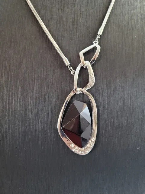 A faceted black gem is nestled inside of a shimmery silver frame enscrusted with white rhinestone. Sold with one pair of matching earrings. 